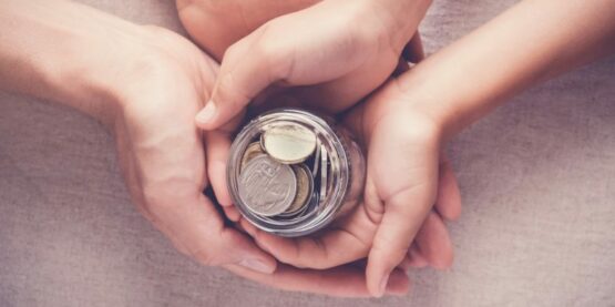 diferentes mãos segurando um potinho com dinheiro representando o ato da doação